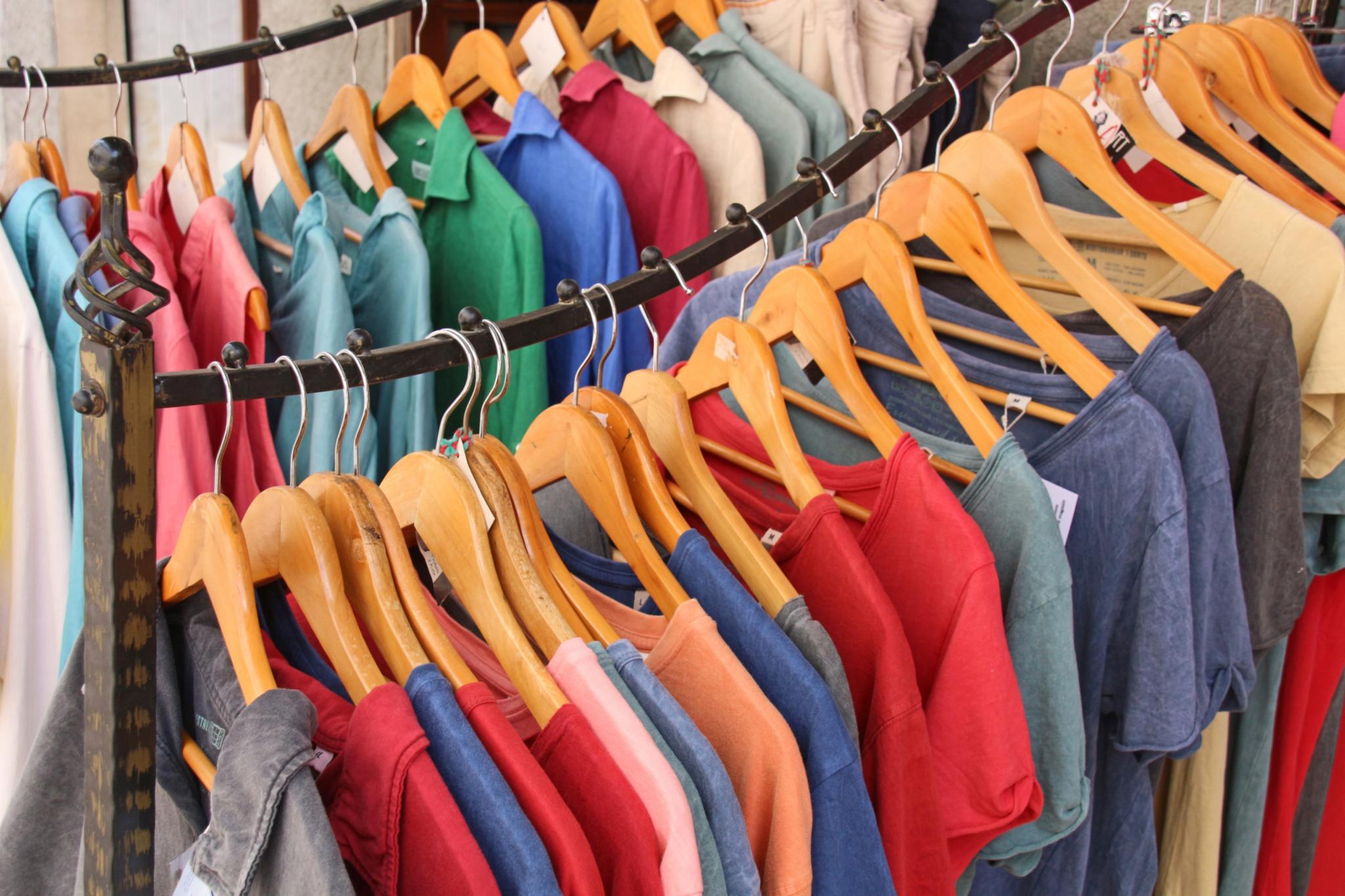 bunte T-Shirts hängen auf Bügeln an zwei gebogenen Kleiderstangen.